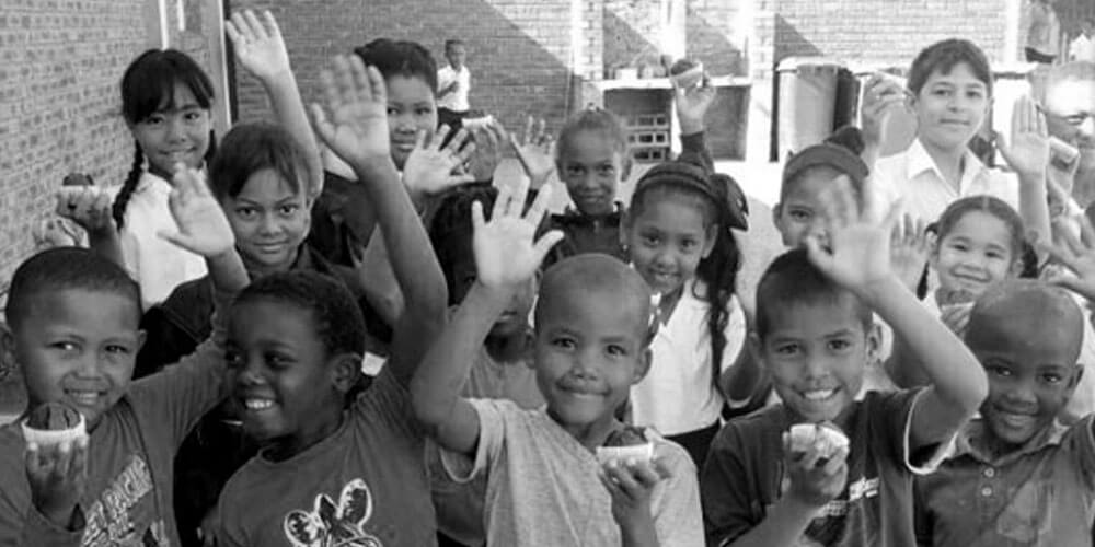 Südafrikanische Kinder mit Magic Muffins in den Händen winken und lachen fröhlich