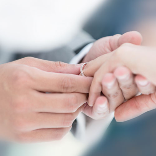 Männliche Hand steckt weiblicher Hand einen goldenen Ring an den Finger