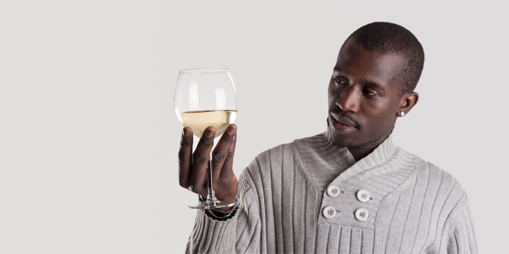 Attraktiver Südafrikaner schaut seitlich in ein gefülltes Weißweinglas